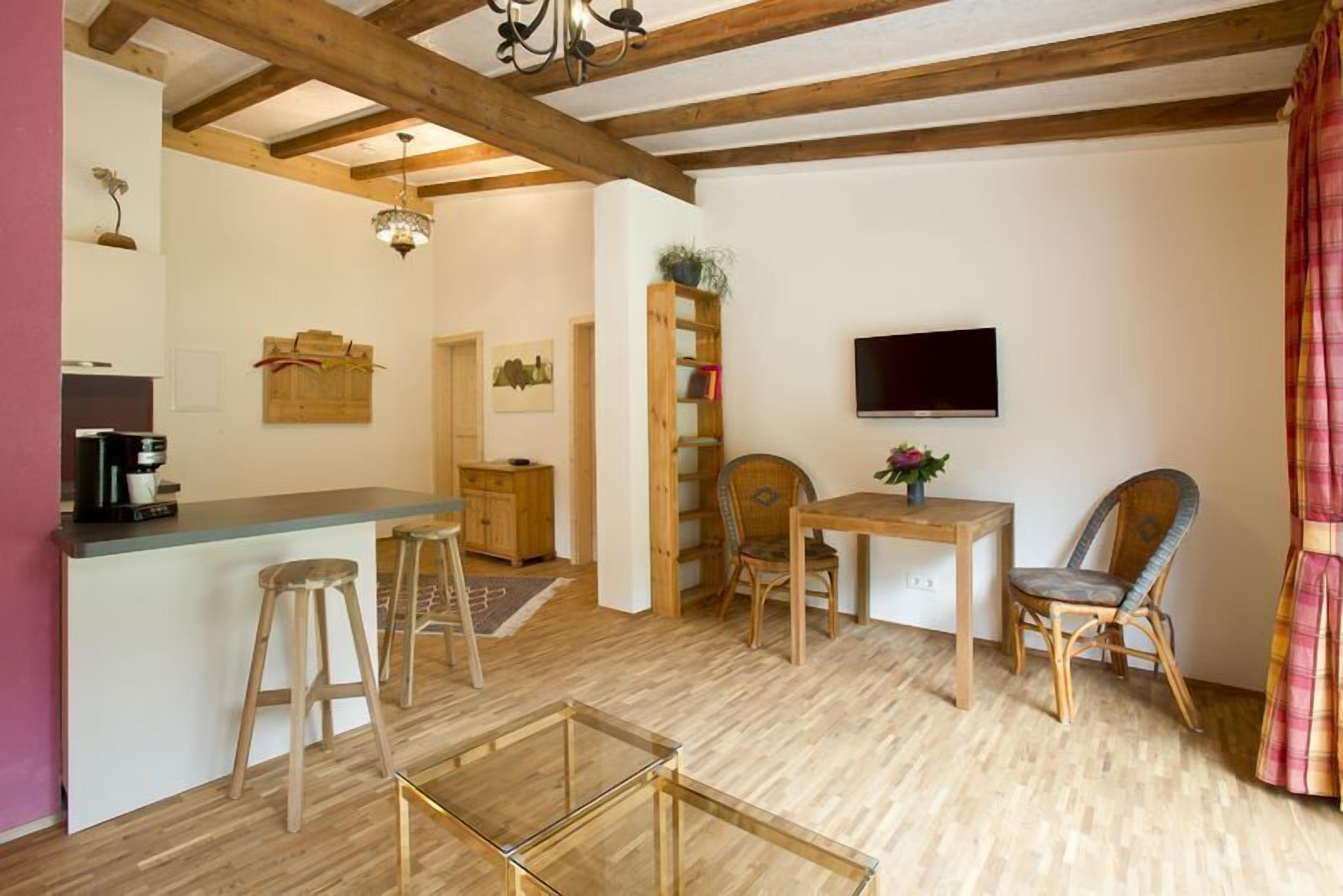 Een gezellige woonruimte met houten plafond, een eettafel, twee stoelen, een televisie en een keuken met krukjes.