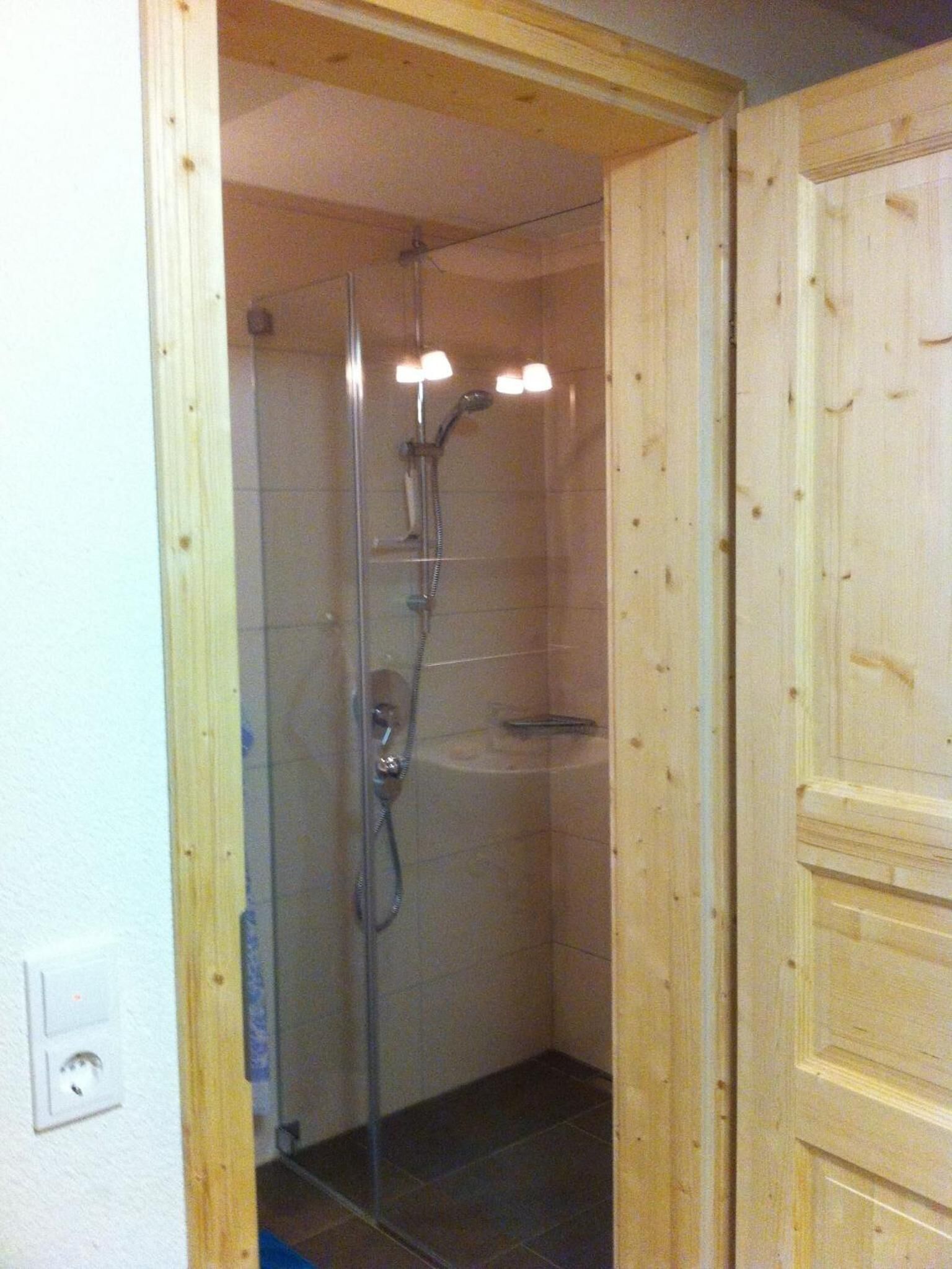 Eine Duschkabine mit Handbrause und verstellbarem Wasserhahn an der Wand.