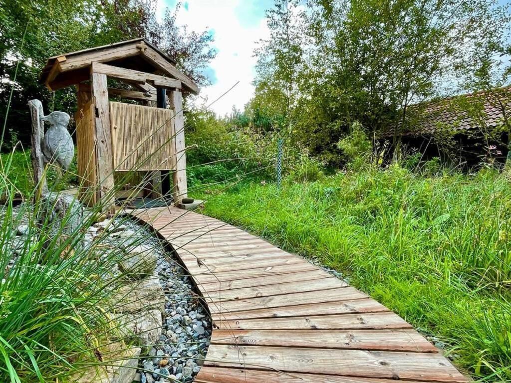 Une structure en bois dotée d’un toit en pente, entourée de verdure et bordée d’un chemin de gravier.