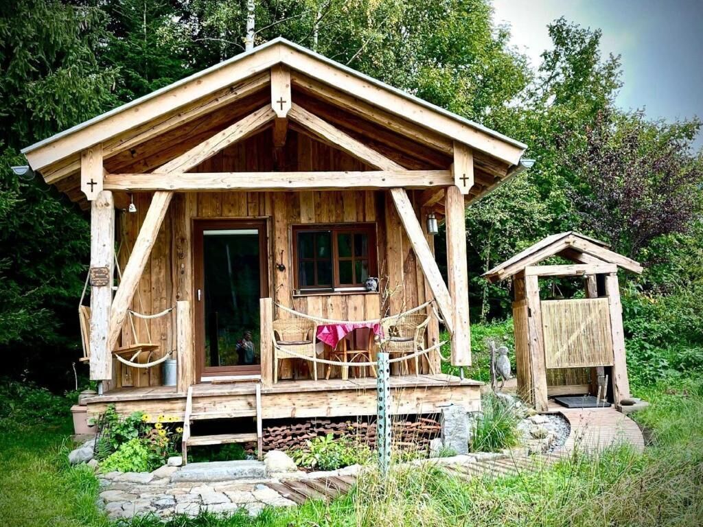 Una cabaña de madera con un porche, una estructura pequeña adosada y un sendero de piedra que lleva a la entrada.