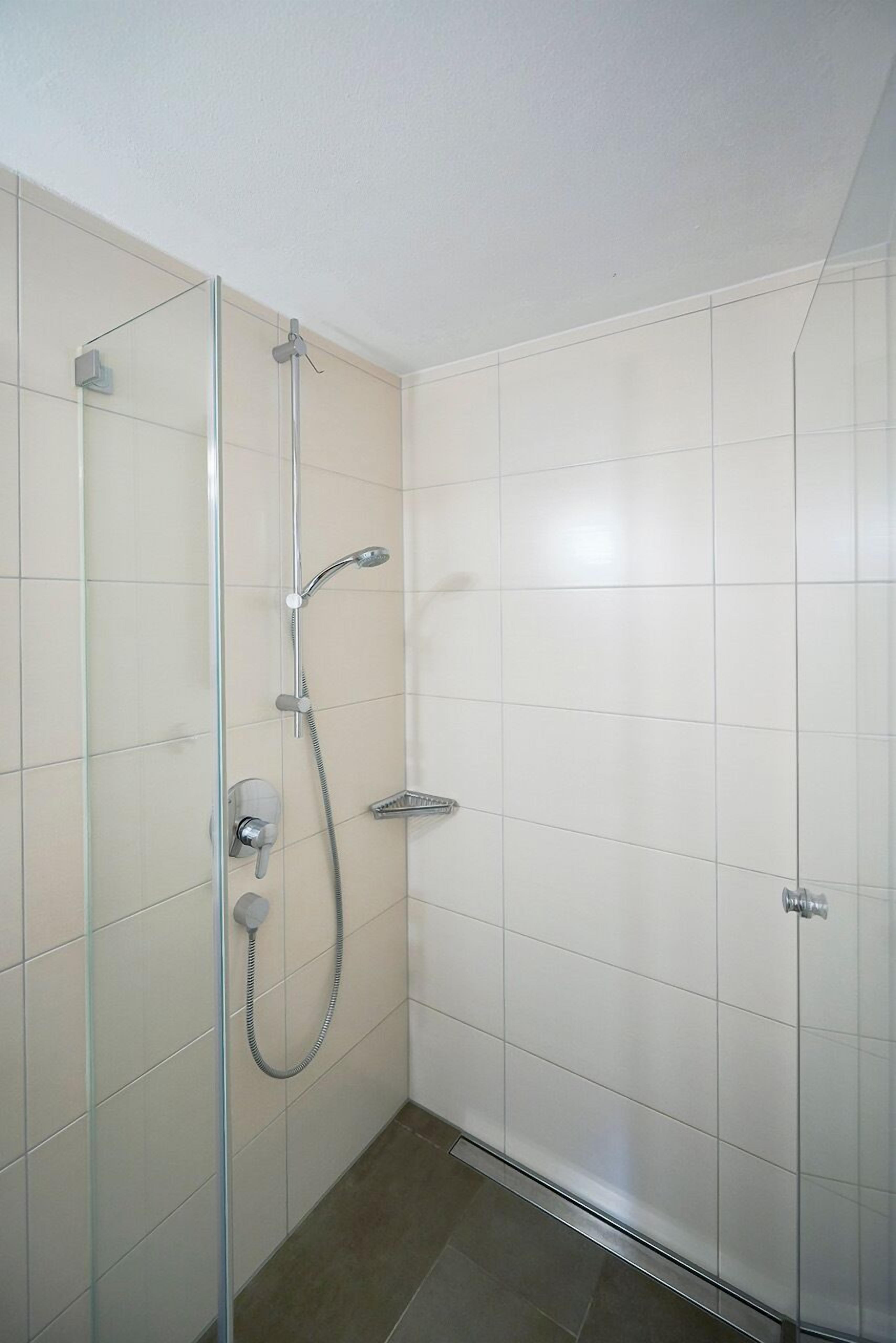 A modern shower with a glass door, a handheld showerhead, and a wall-mounted control panel.