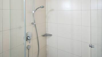 A modern shower with a glass door, a handheld showerhead, and a wall-mounted control panel.