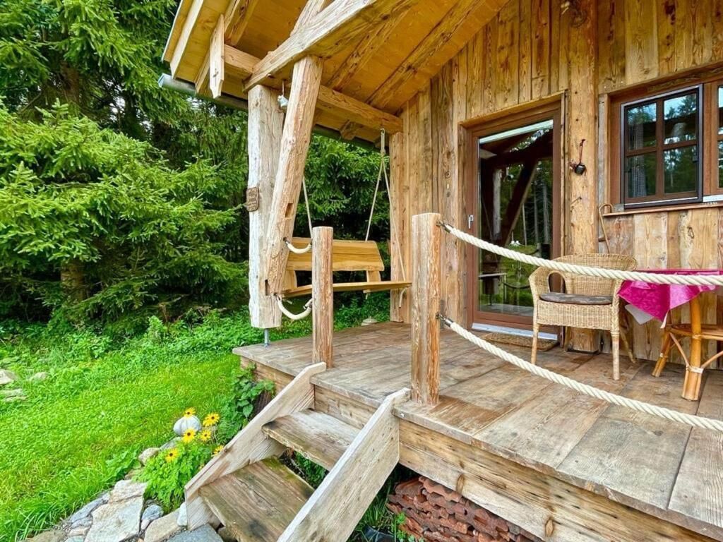 A wooden cabin with a porch, a dining area with a table and chairs, and a stone wall.