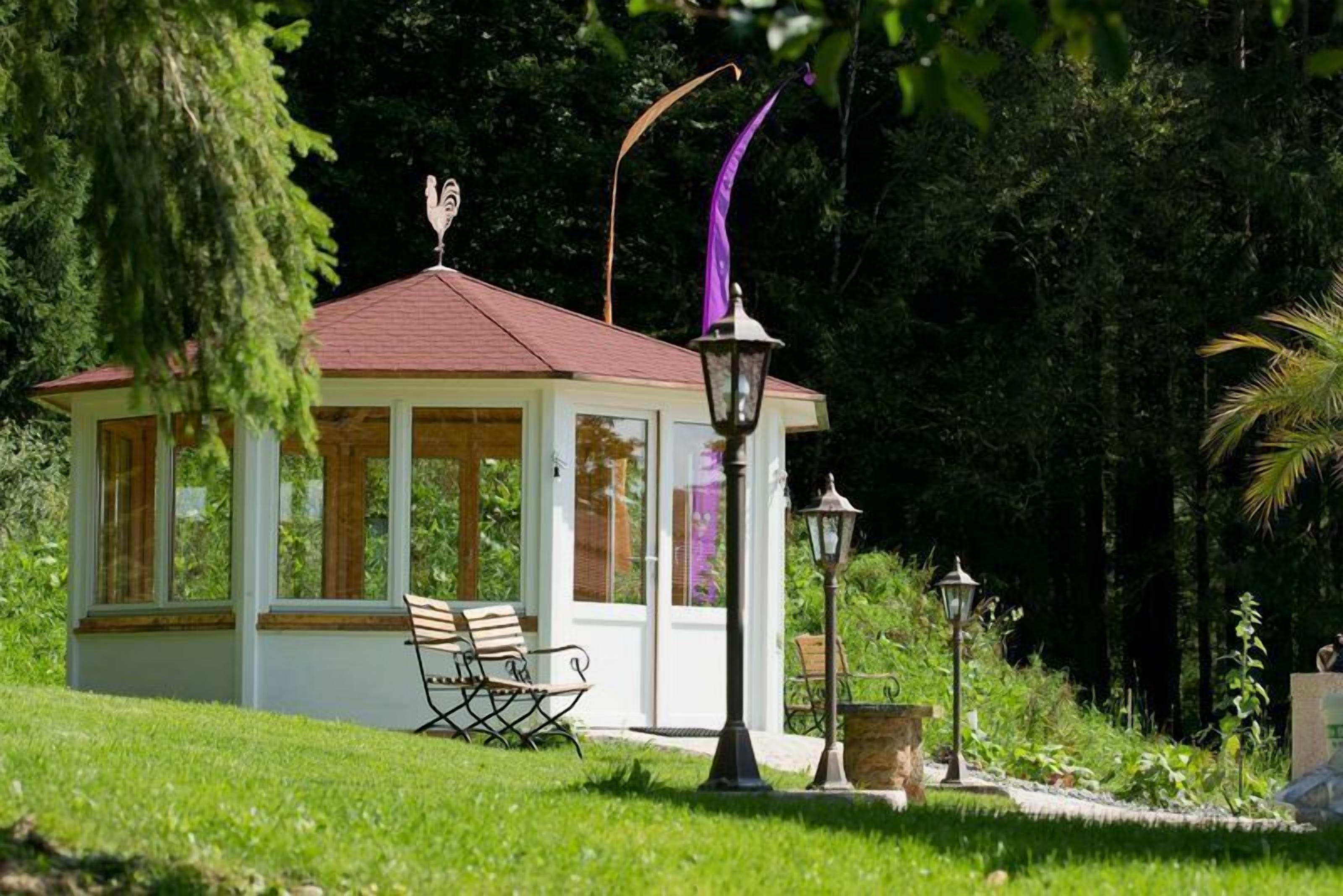 Un petit kiosque avec un toit rouge, un banc et deux lampadaires, le tout situé dans un jardin luxuriant.
