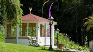 Un petit kiosque avec un toit rouge, un banc et deux lampadaires, le tout situé dans un jardin luxuriant.