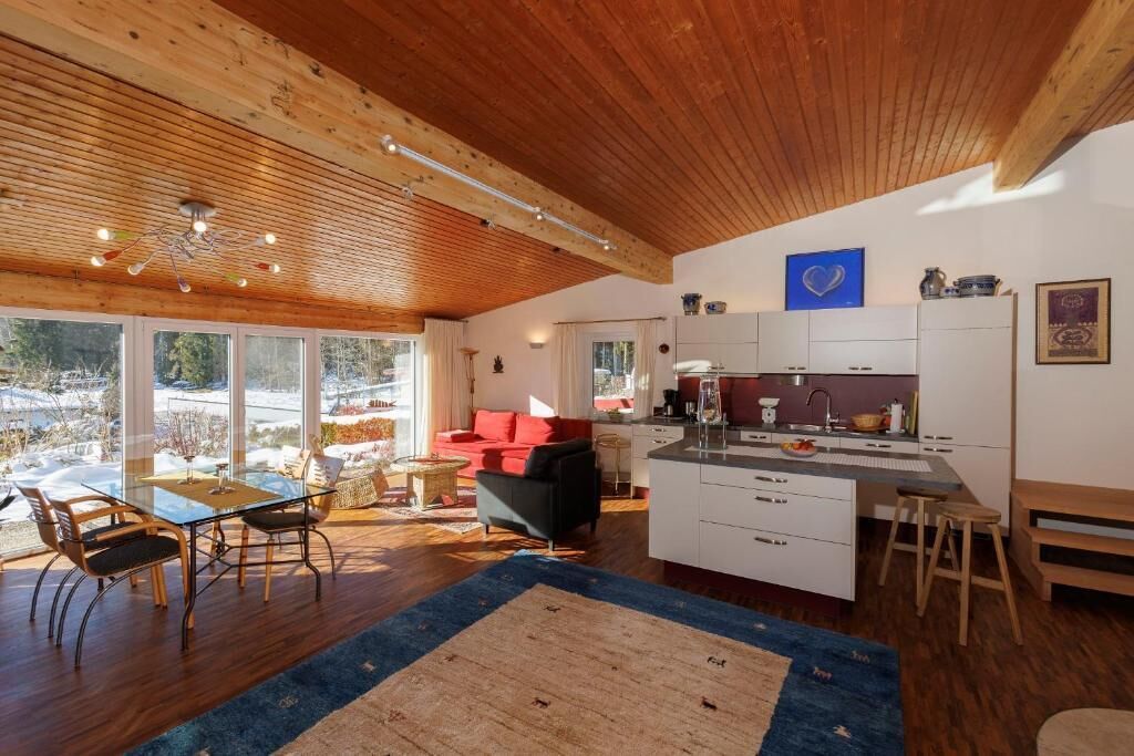 Une cuisine moderne avec des meubles blancs, un îlot central et un coin repas comprenant une table et des chaises en verre.