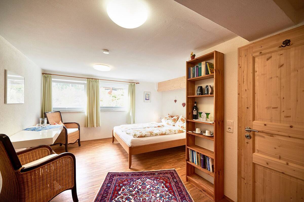 Une chambre confortable avec un lit, une bibliothèque en bois, une table à manger avec des chaises et une fenêtre avec des rideaux.