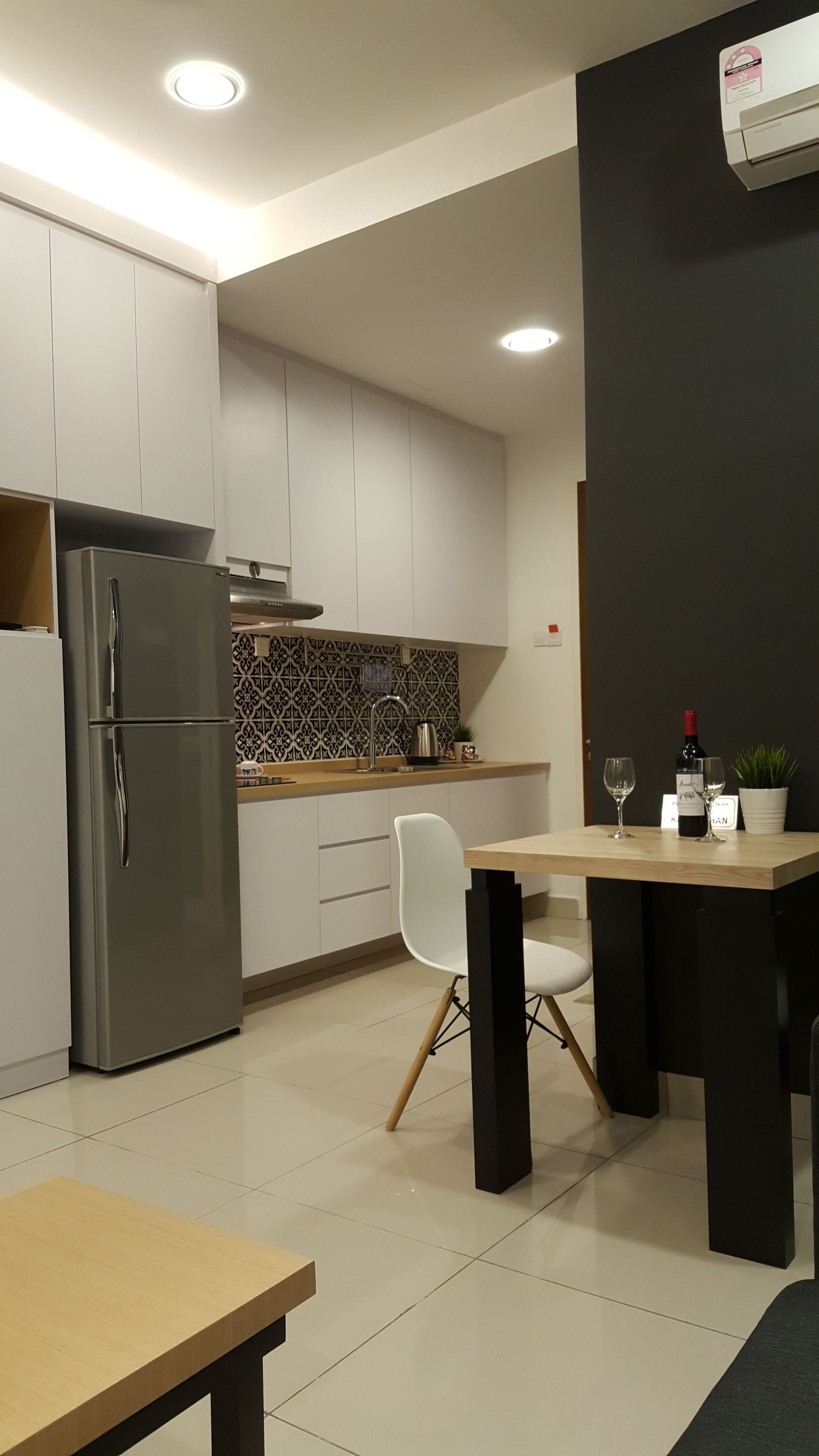 A modern kitchen with white cabinets, a stainless steel refrigerator, a black countertop, and a dining area with a table and chairs.