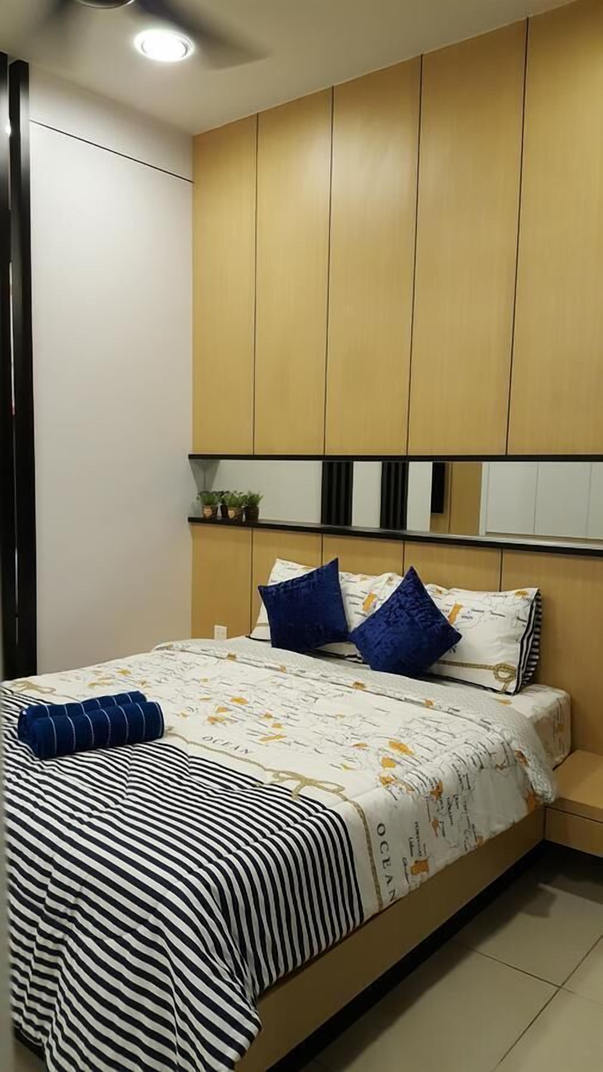Quarto com cama, almofadas, mesa de cabeceira e prateleira com plantas.