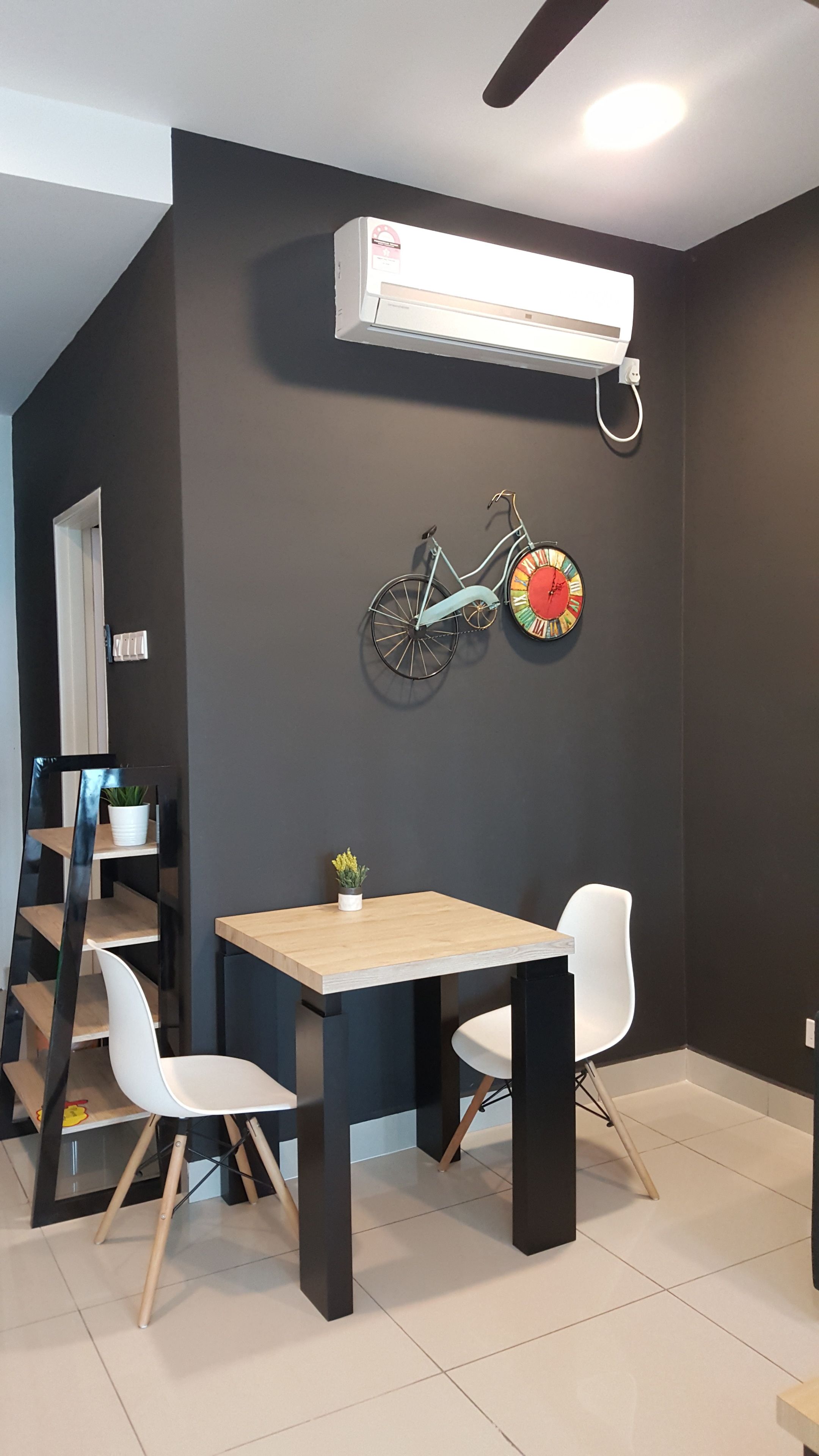 Un comedor moderno con una mesa de madera y dos sillas blancas, una bicicleta de estructura negra y un aire acondicionado fijado a la pared.