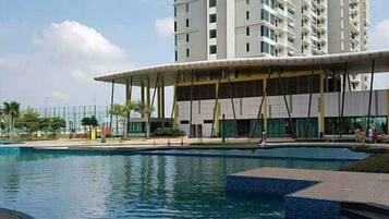 Un hotel moderno con zona de piscina, un pabellón cubierto y un edificio alto al fondo.