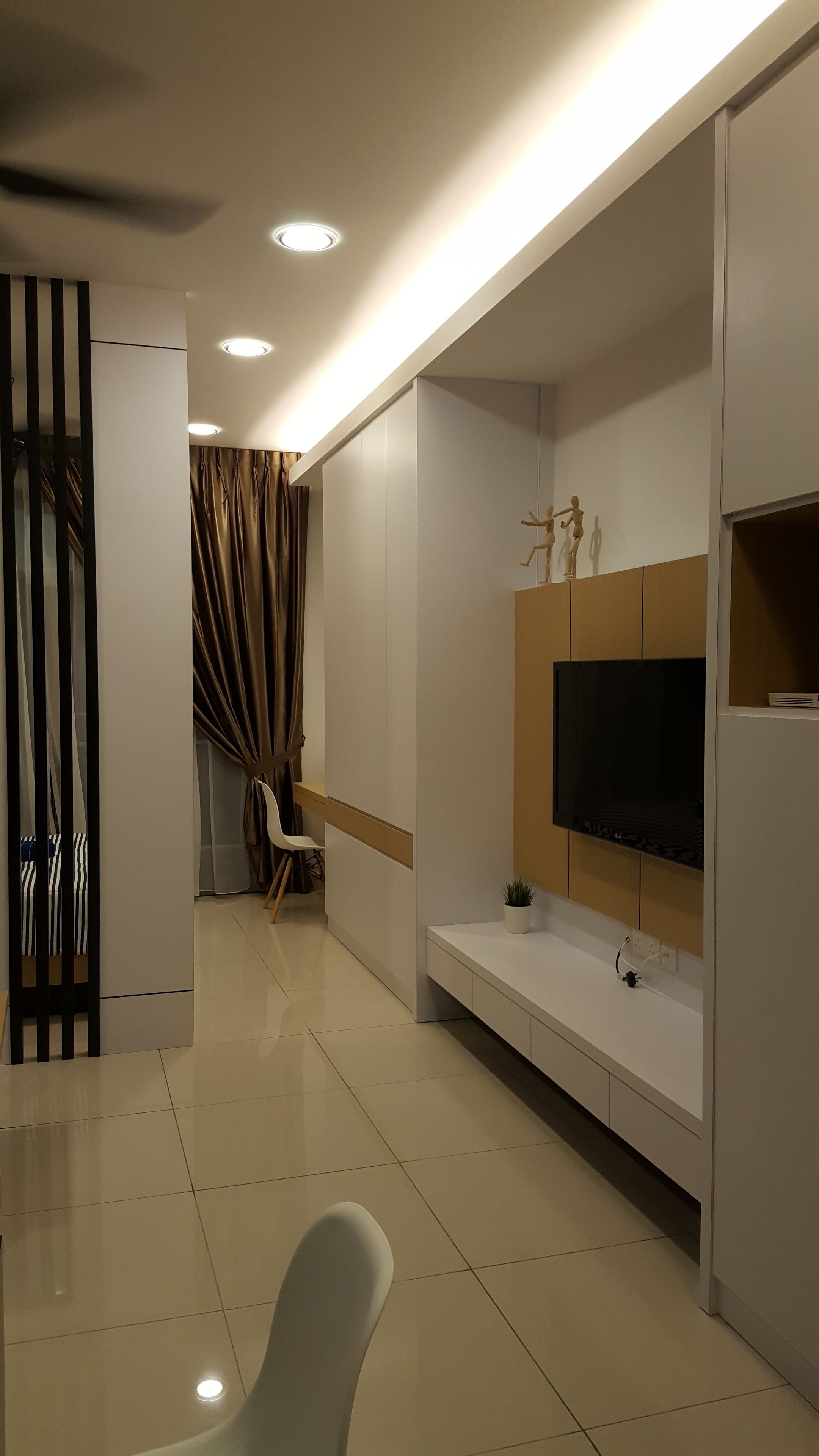 Una sala de estar moderna con un televisor de pantalla plana montado en un panel de madera, un sofá blanco y una pequeña mesa con una planta.