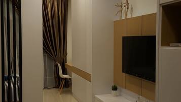 Una sala de estar moderna con un televisor de pantalla plana montado en un panel de madera, un sofá blanco y una pequeña mesa con una planta.