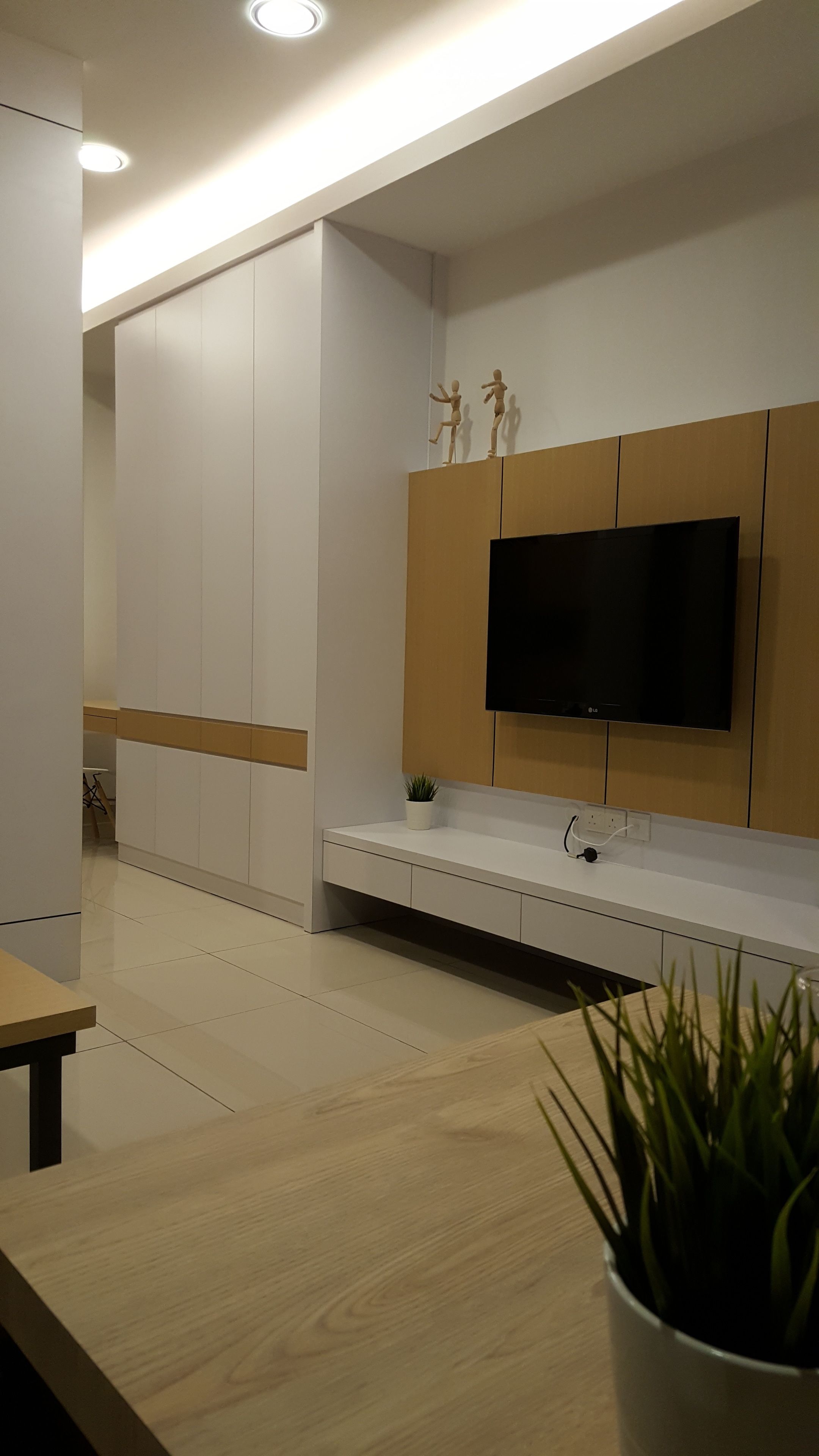Ein modernes Wohnzimmer mit einem Flachbildfernseher, der an einer Wand aus Holzpaneelen angebracht ist, einer weißen Kommode mit einer Pflanze und einem Holztisch.