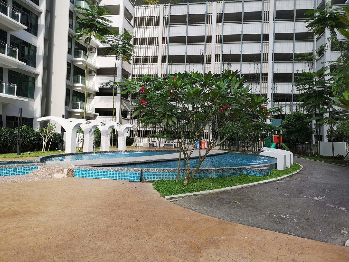 A modern building with a swimming pool, surrounded by greenery and a paved walkway.