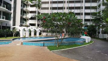 A modern building with a swimming pool, surrounded by greenery and a paved walkway.