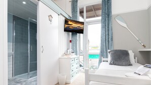 A modern hotel room with a glass shower, a bed with a pillow, a mounted TV, and a paddle on the wall. - Beachside Guest House (Llandudno)