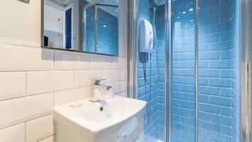 Un baño moderno con un lavamanos blanco, una cabina de ducha con mampara de vidrio y paredes cubiertas de azulejos azules.