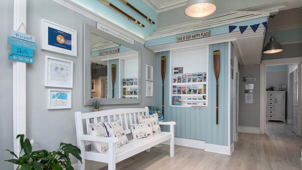 A reception area with a white bench, framed welcome signs, a bookshelf with books, and a mirror reflecting the room. - Beachside Guest House (Llandudno)