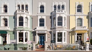 A row of colorful townhouses with distinct architectural features, including bay windows and decorative moldings. - Beachside Guest House (Llandudno)