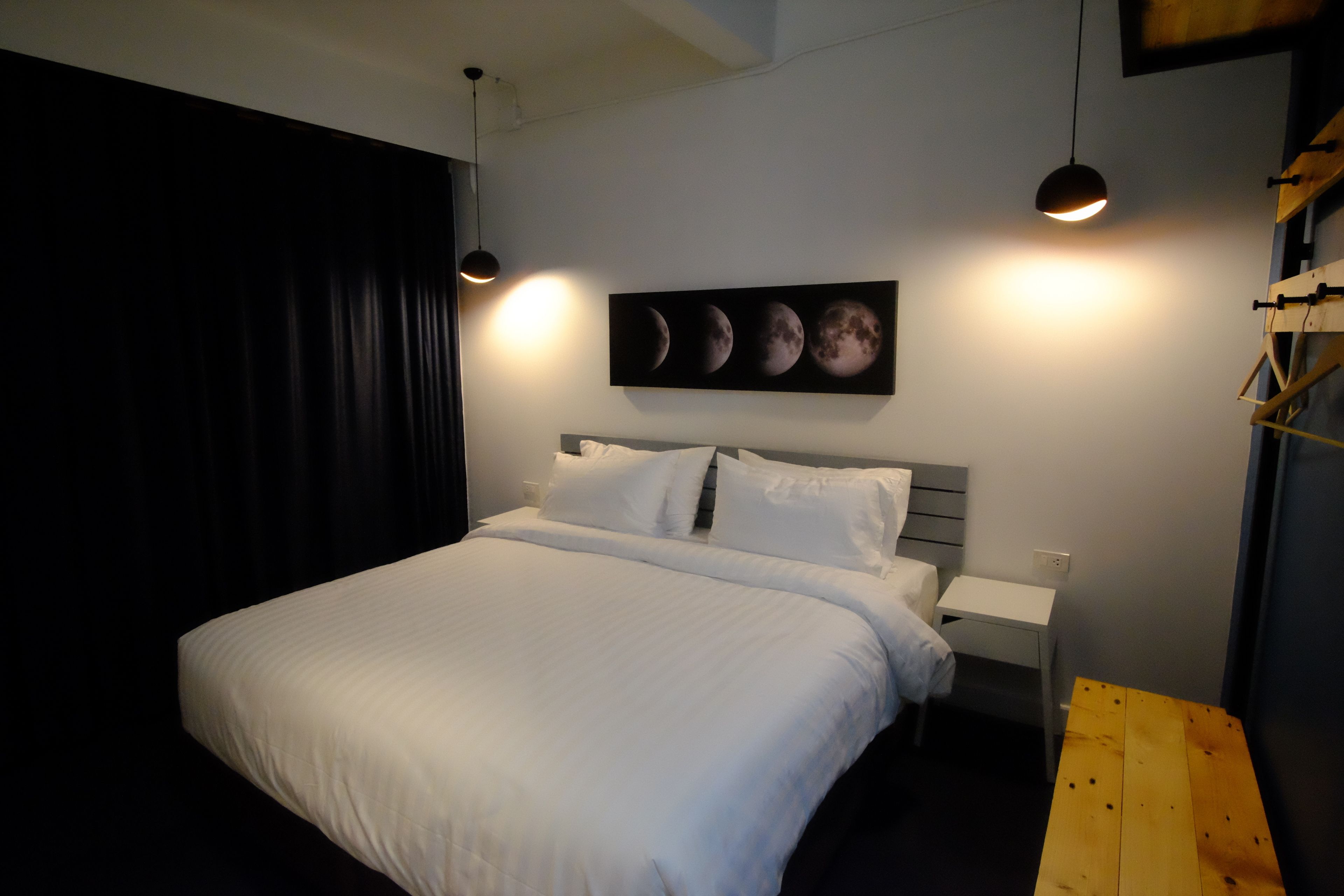 Una camera da letto con un letto, un comodino, una panca di legno e un quadro a parete raffigurante le fasi lunari.