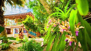 A traditional wooden structure with a balcony, surrounded by lush greenery and flowering plants. - Eco Hotel Las Palmas (Armenia)