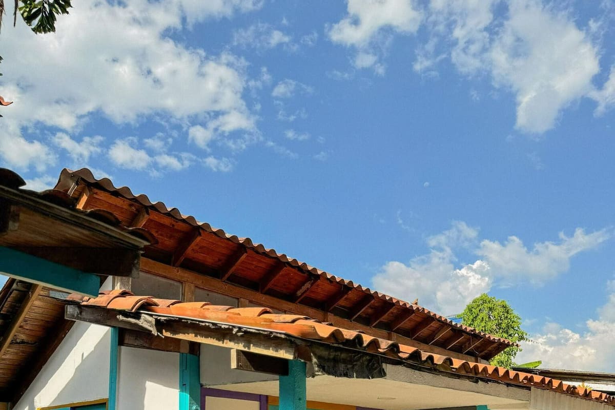 Un edificio colorido con techo de tejas, un porche con banca y plantas en macetas.