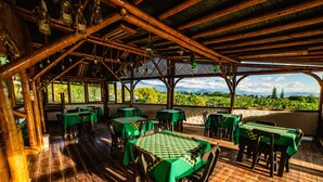 An outdoor restaurant with bamboo structures, green tables, and chairs, overlooking a lush landscape. - Eco Hotel Las Palmas (Armenia)