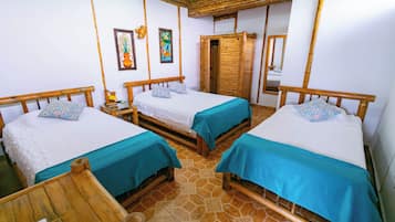 Quarto com três camas de madeira, cada uma com colcha azul e almofadas estampadas. Há duas luminárias fixadas na parede e uma porta de madeira.