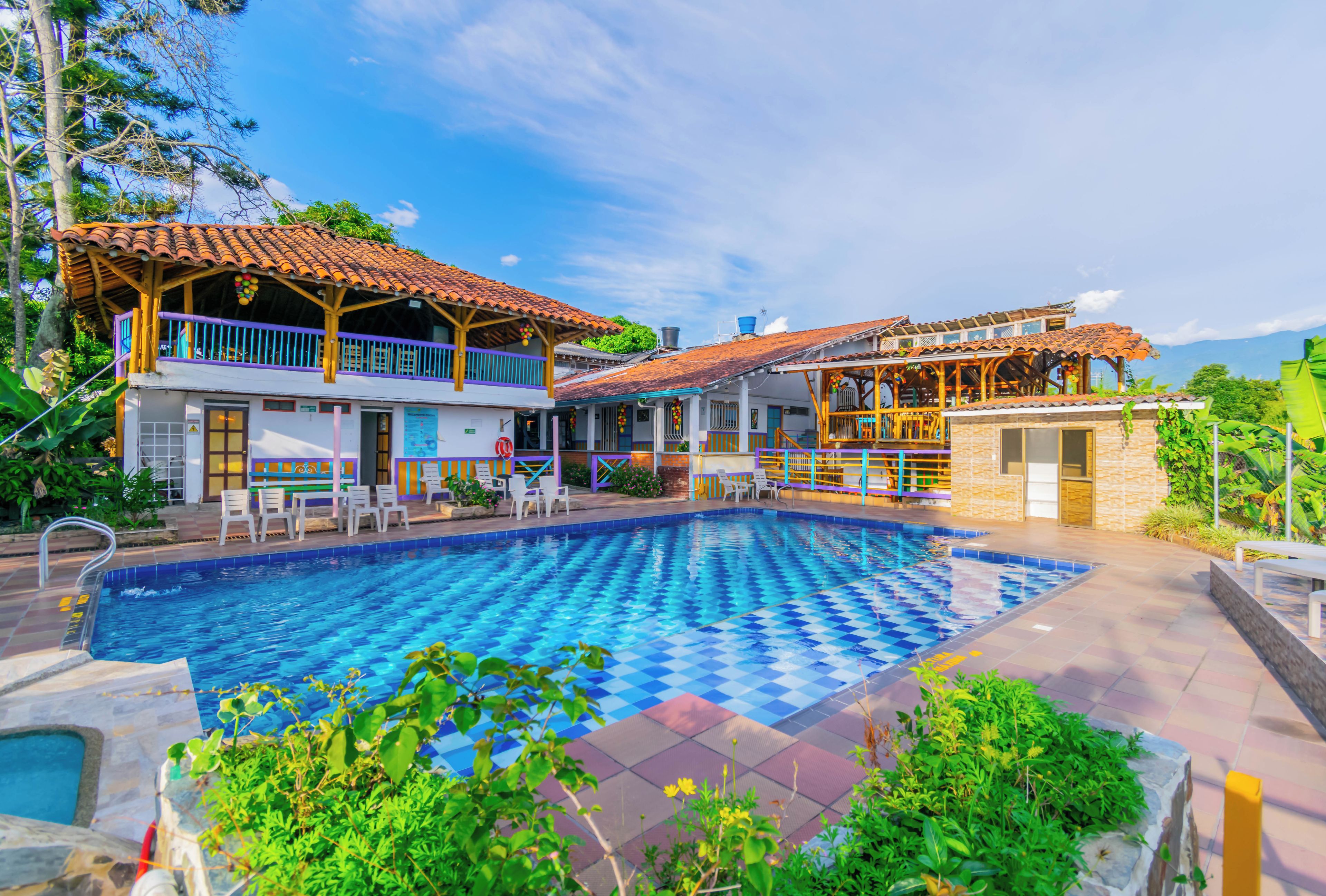 A large outdoor swimming pool with a checkered pattern, surrounded by a patio area with outdoor seating and a view of the mountains.