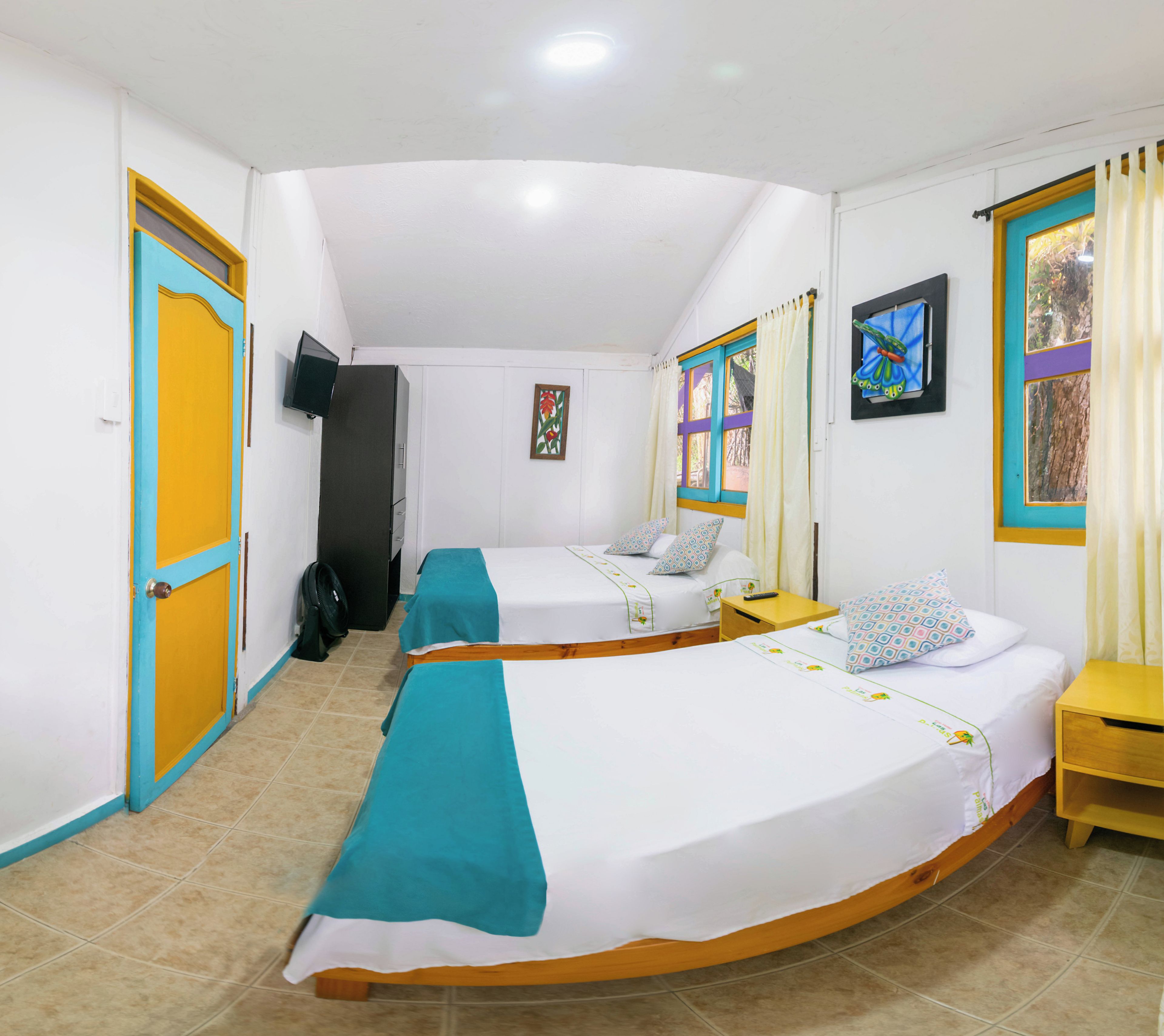 A hotel room with two beds, a television, a wardrobe, and a window with curtains.