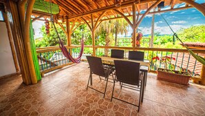 An outdoor patio with a bamboo ceiling, a table with chairs, and a view of lush greenery. - Eco Hotel Las Palmas (Armenia)