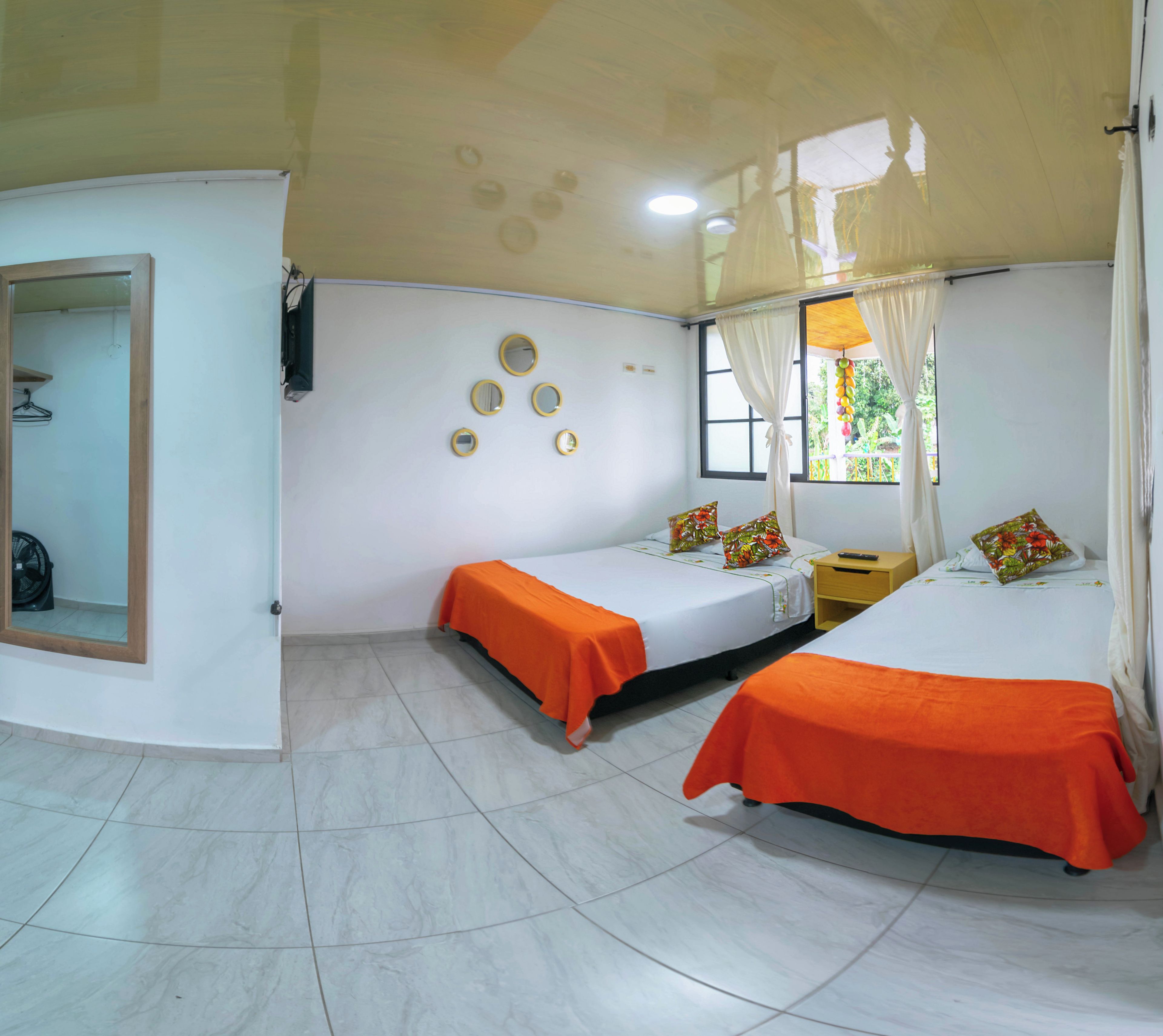 A hotel room with two beds, a mirror, a fan, and a window with curtains.