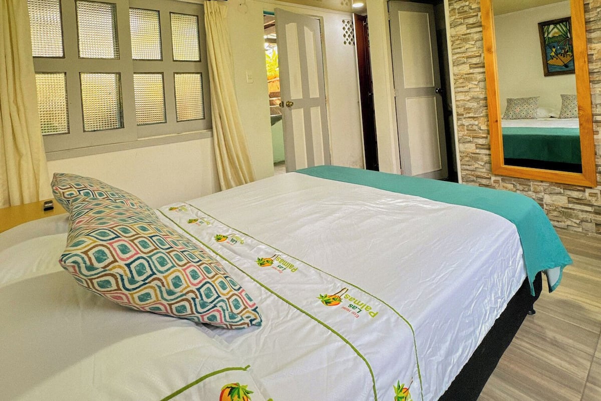 Habitación de hotel con una cama, una ventana con cortinas, una puerta y una pared de piedra con un espejo.