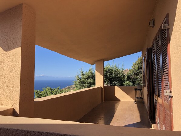 Ein überdachter Balkon mit Blick auf das Meer und die grüne Landschaft.