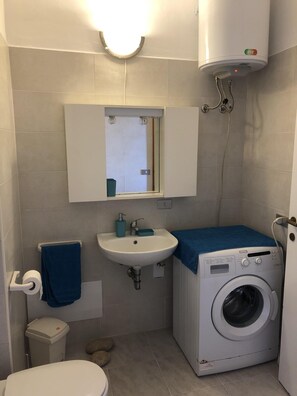 Ein kleines Badezimmer mit Waschbecken, Spiegel, Toilette und Waschmaschine.