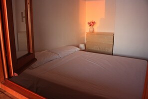 Ein ordentlich bezogenes Bett mit weißen Leinen in einem Zimmer mit einem Holzkasten und einer Vase mit Blumen darauf.