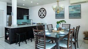 Een moderne keuken met donkere kastjes, een centraal eiland en een eethoek met een glazen tafel en houten stoelen.