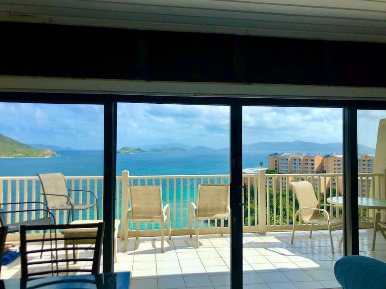 A balcony with chairs and a table, overlooking a coastal view with buildings in the distance.