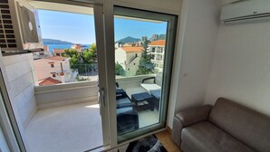 En balkon med glasdør, en beige sofa og udsigt over et bybillede med bygninger og et bjerg.