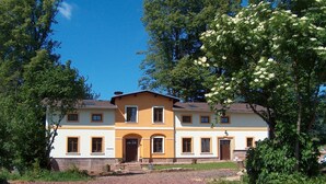 A two-story house with a symmetrical facade, a central entrance with a door, and a gravel driveway. - Nostalgic renovated farmhouse in beautiful surroundings (Božanov)