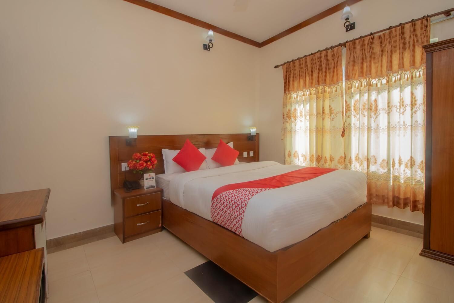 A hotel room with a wooden bed, a nightstand, a desk, and a window with curtains.