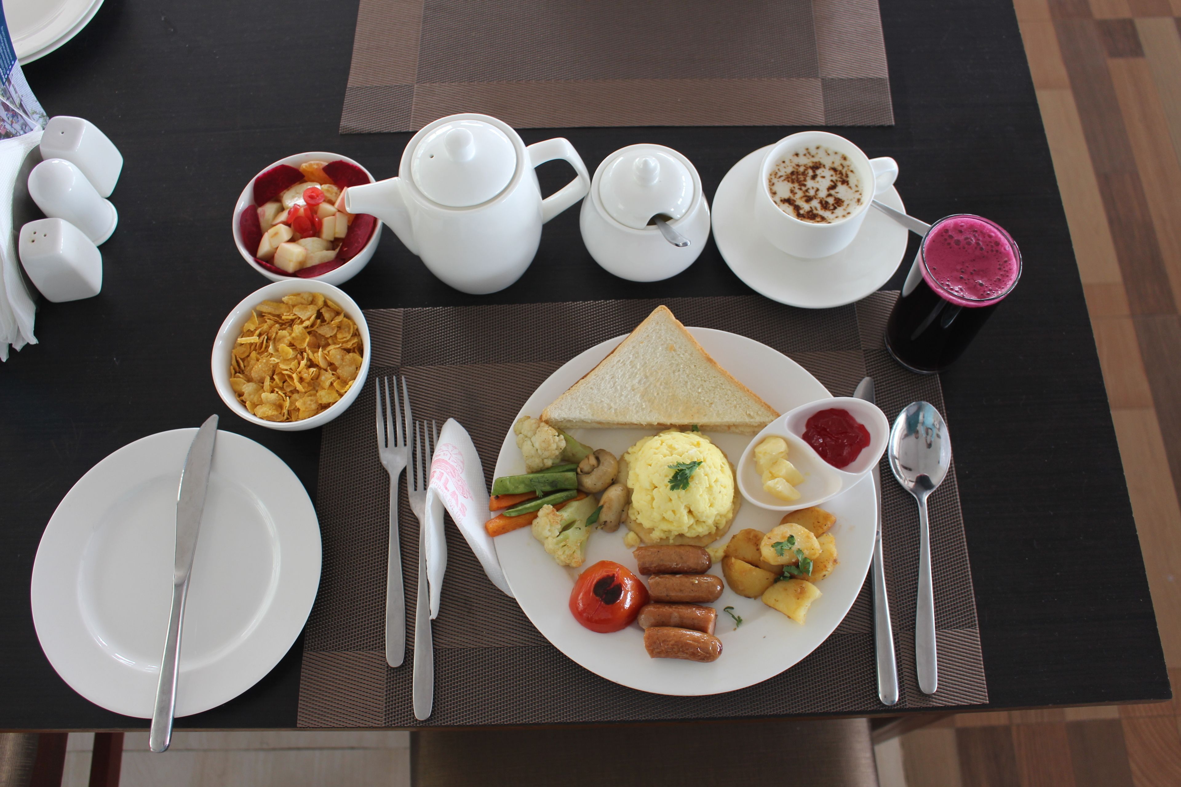 A breakfast table with a variety of food items including toast, scrambled eggs, sausages, and vegetables.