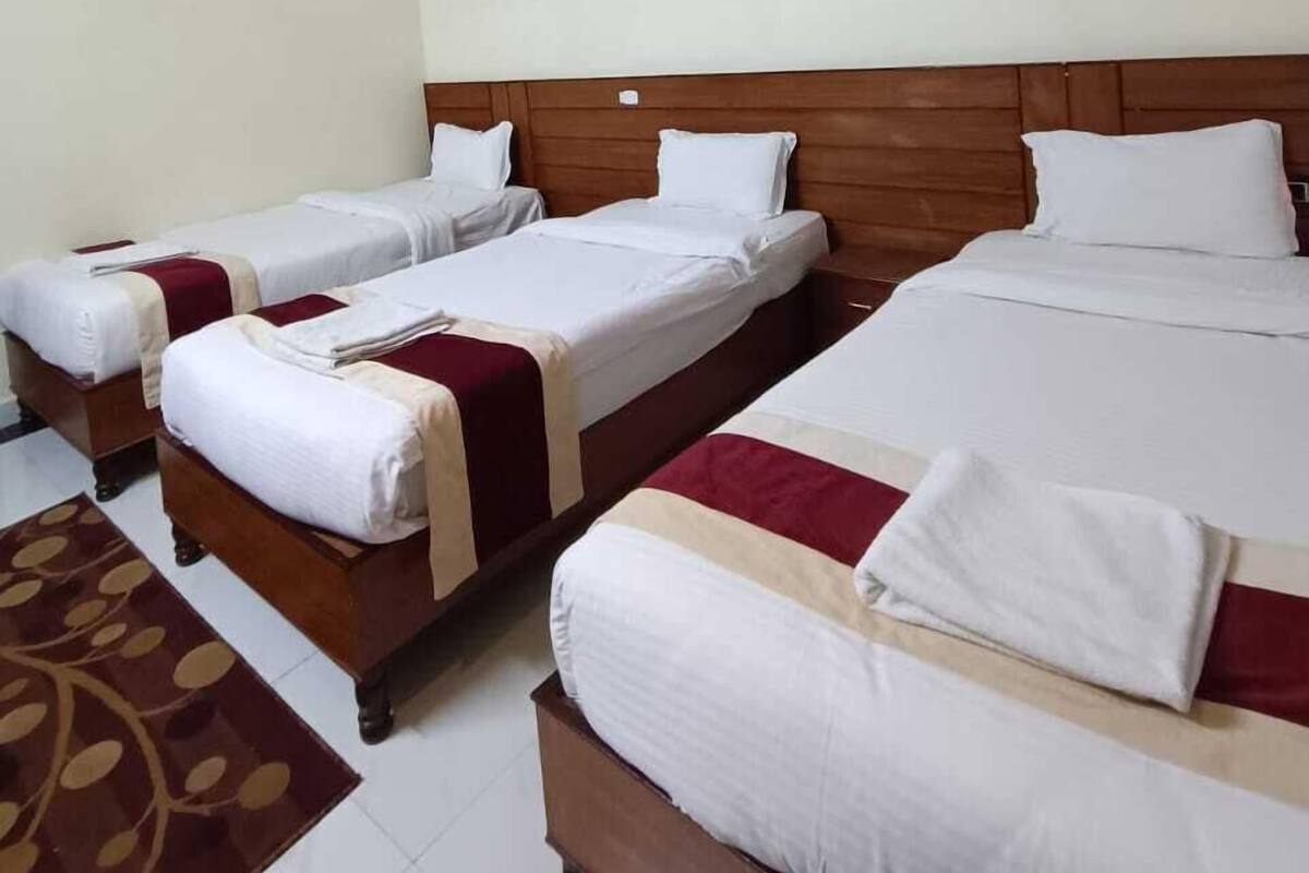 A hotel room with three beds, a wooden headboard, a ceiling fan, and a patterned floor rug.