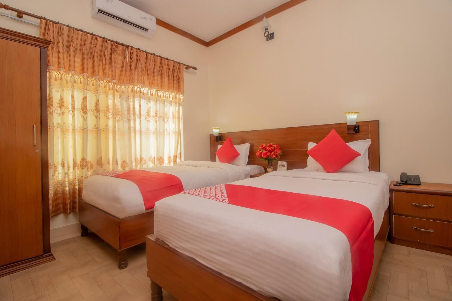 A hotel room with two beds, a wooden wardrobe, a nightstand with a phone, and a window with curtains.