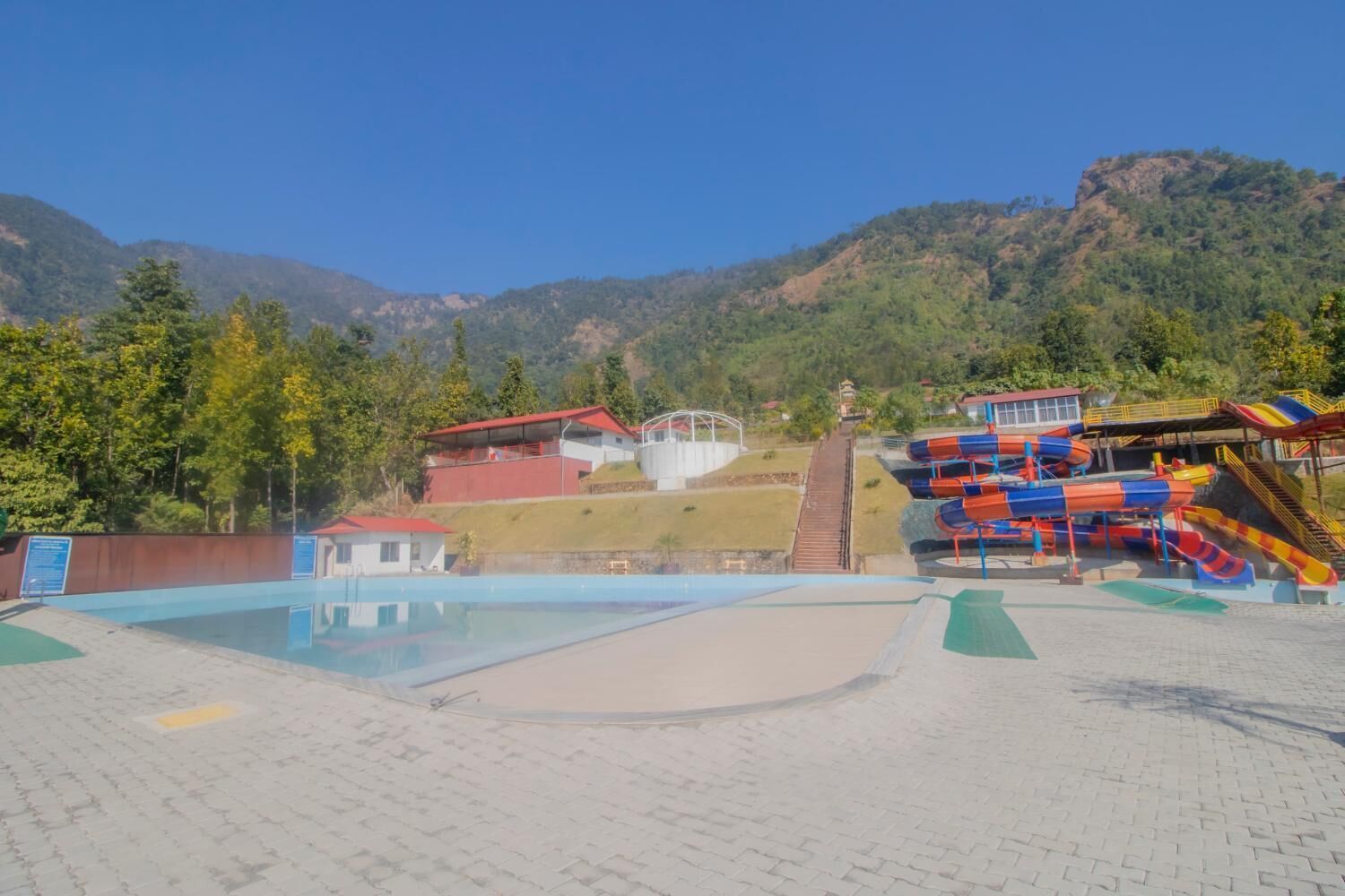 A swimming pool area with a water slide and a small building with a red roof.