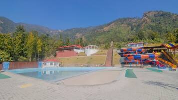 A swimming pool area with a water slide and a small building with a red roof.