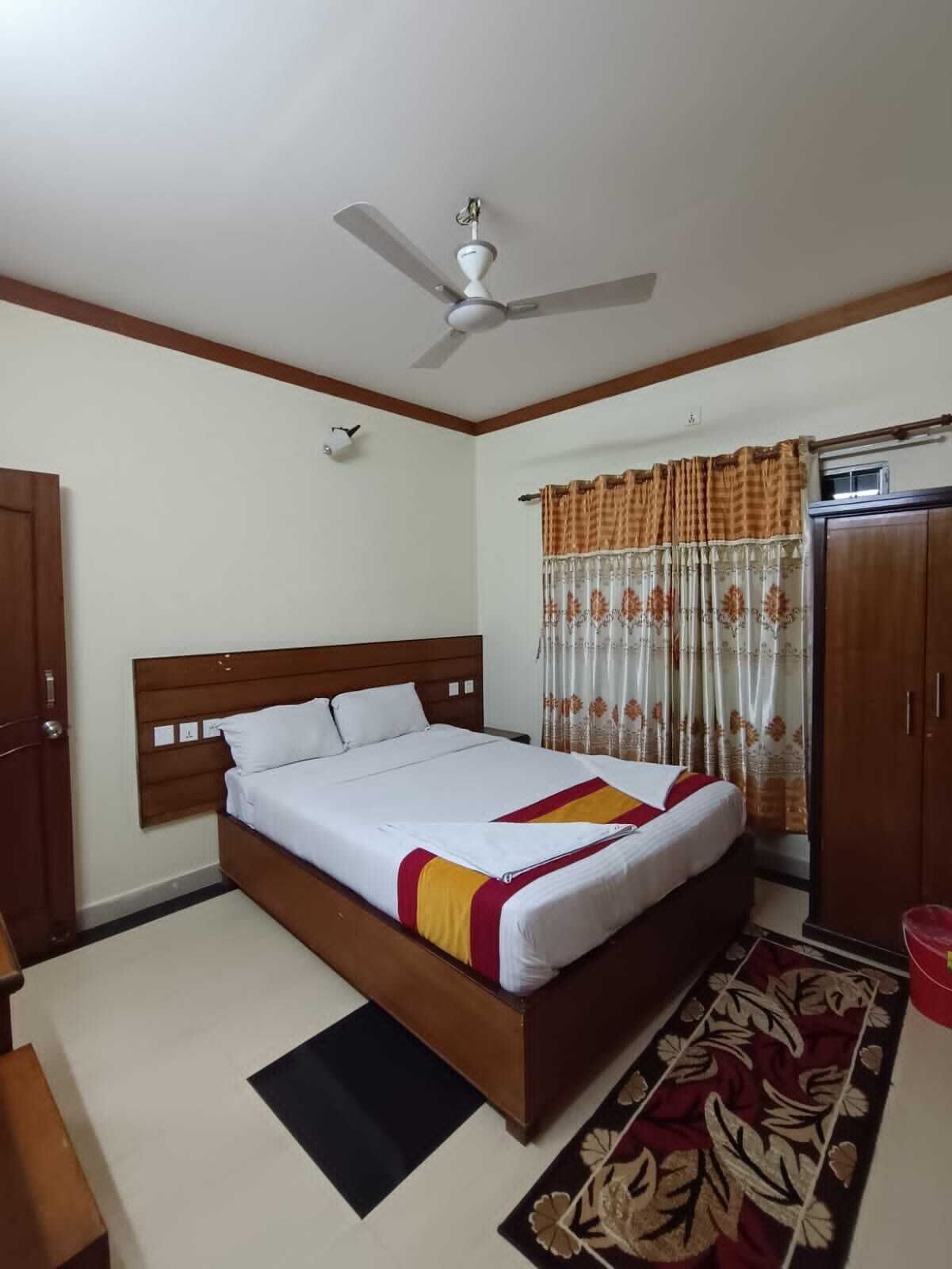A bedroom with a bed, a ceiling fan, a wardrobe, and a window with curtains.