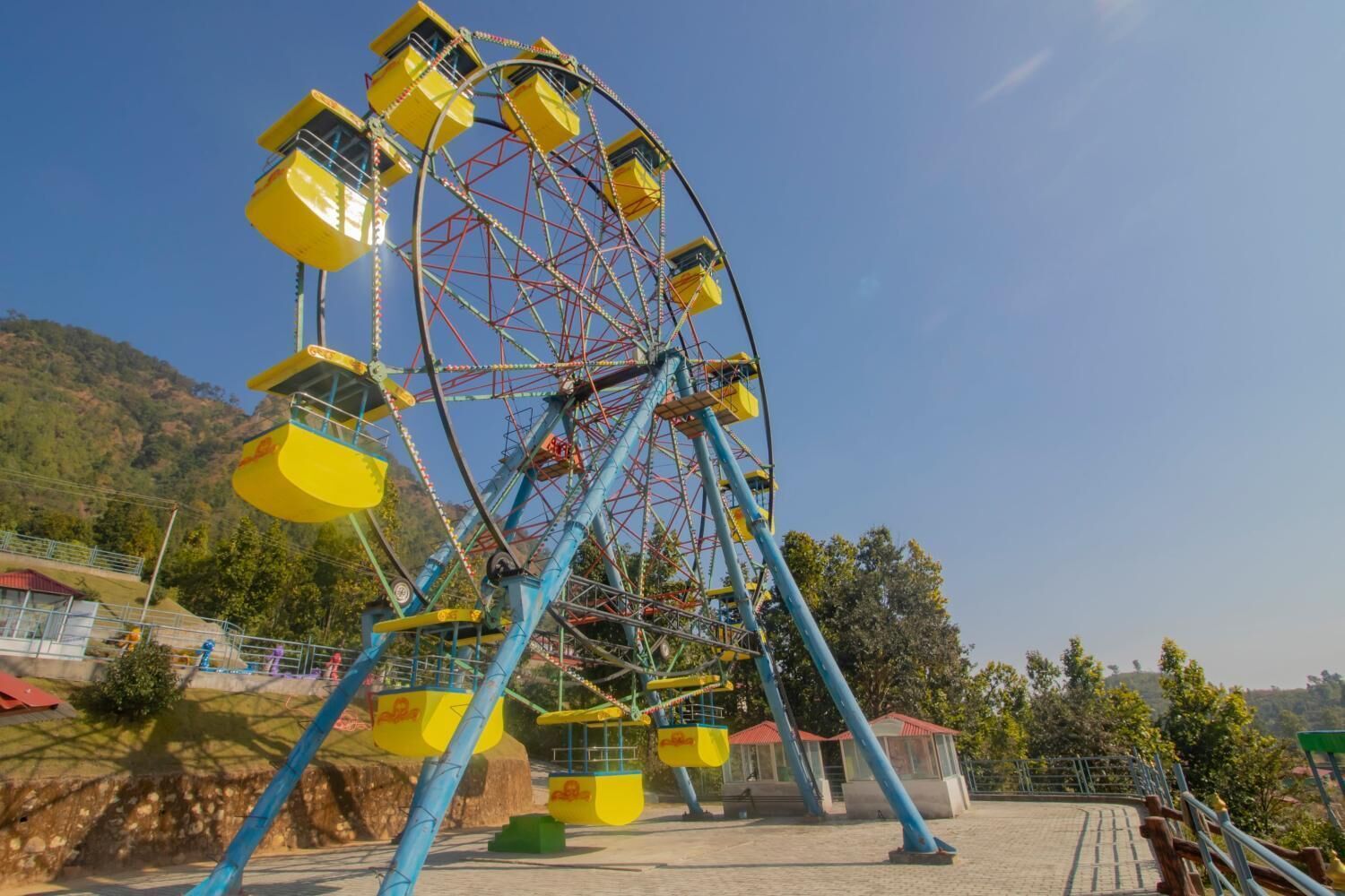 A large Ferris wheel with yellow cabins, set against a backdrop of trees and hills.