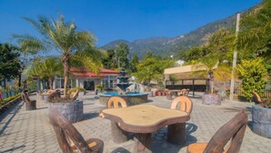 An outdoor patio with a wooden table and chairs, surrounded by potted plants and a fountain. - Kabilas Resort and Funpark (Kabilas)